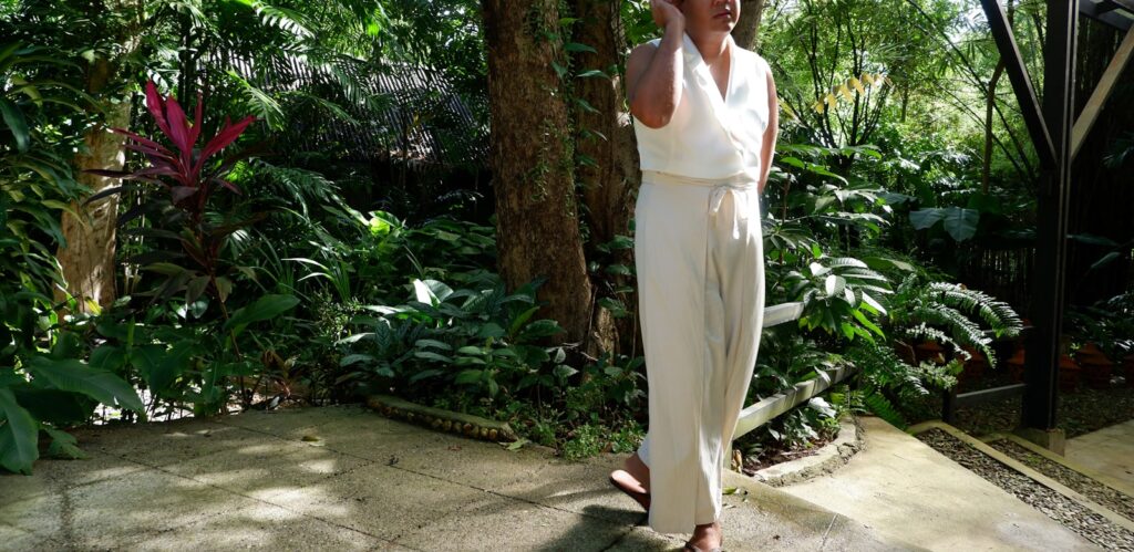 Woman in white outfit standing in a lush garden.